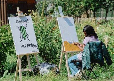 Kind malt an einer Staffelei zwischen Pflanzen beim Sommerferienprogramm von Ackerperlen